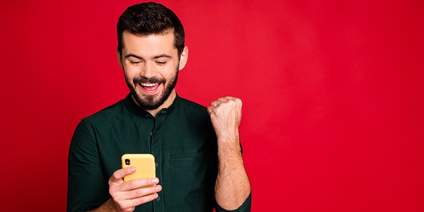 portrait of delighted crazy guy use smartphone read social media lottery win news find sales discount scream yeah raise fists wear modern outfit